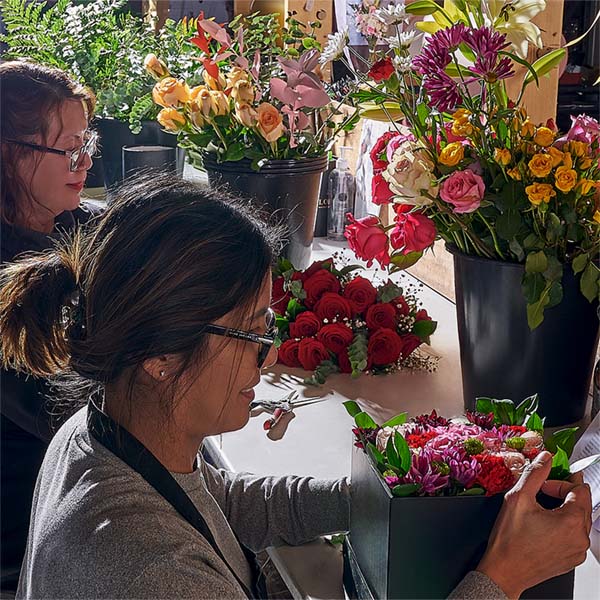 Two women arranging flowers in a floral shop with various flower arrangements on display.