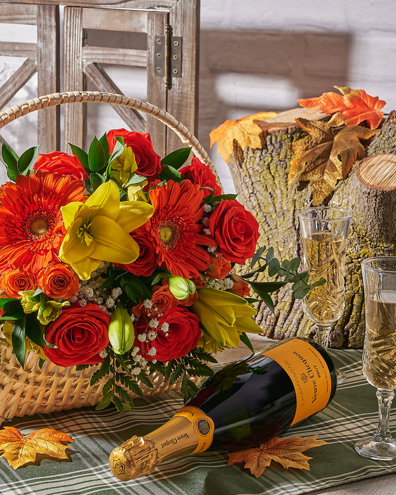 Bouquet of flowers, bottle of champagne, and glasses on a table with autumn decorations.