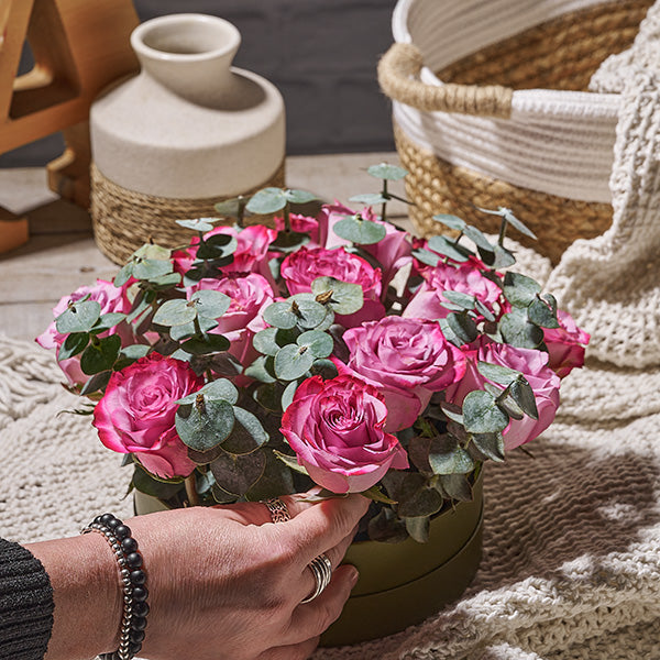 Hand holding a hat box arrangement with purple flowers and eucalyptus leaves.