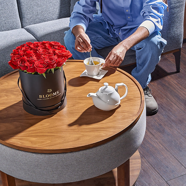 Person sitting on a couch with a table displaying a bouquet of red roses from Toronto Blooms