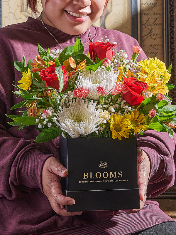 Person holding a floral of flowers in a box labeled 'BLOOMS given same day delivery